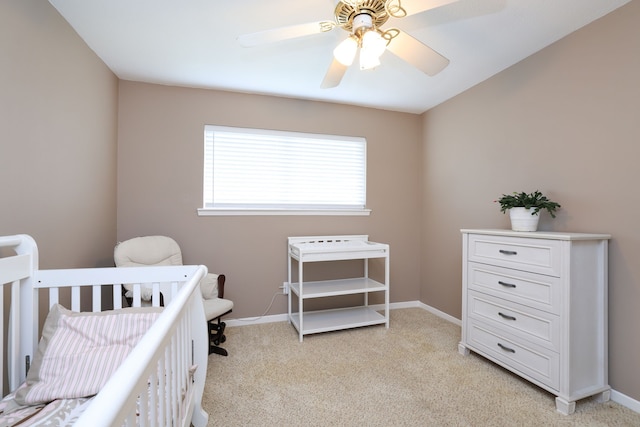 bedroom featuring baseboards, a crib, light colored carpet, and ceiling fan