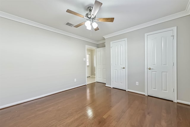 unfurnished bedroom featuring visible vents, baseboards, wood finished floors, and ornamental molding