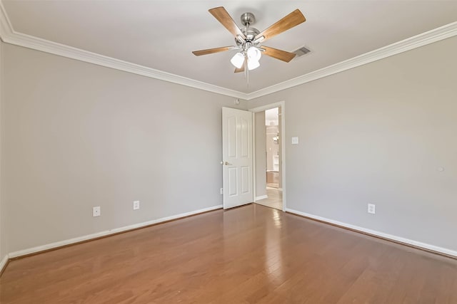 empty room featuring a ceiling fan, wood finished floors, visible vents, baseboards, and crown molding