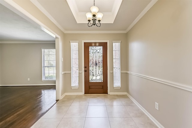 foyer entrance featuring baseboards, a tray ceiling, light tile patterned flooring, crown molding, and a notable chandelier