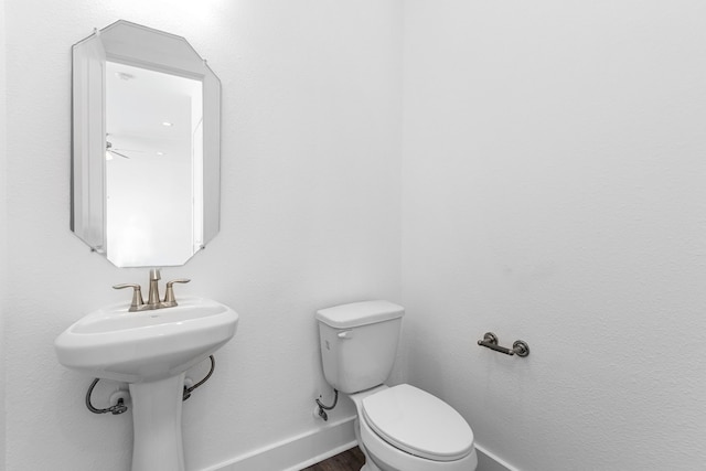 half bath with baseboards, toilet, and wood finished floors