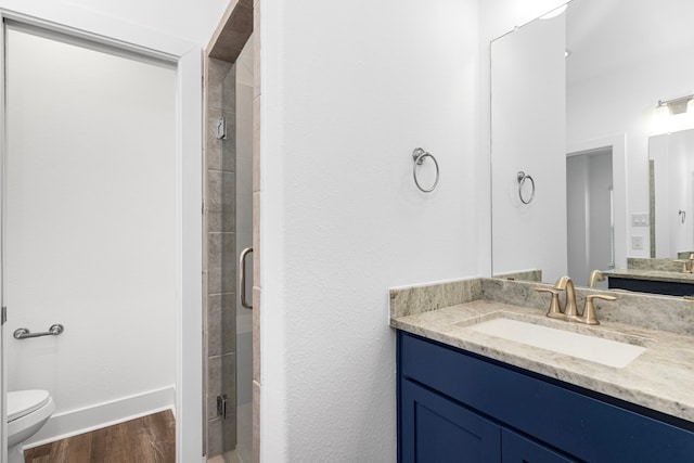 bathroom featuring toilet, wood finished floors, a shower stall, baseboards, and vanity