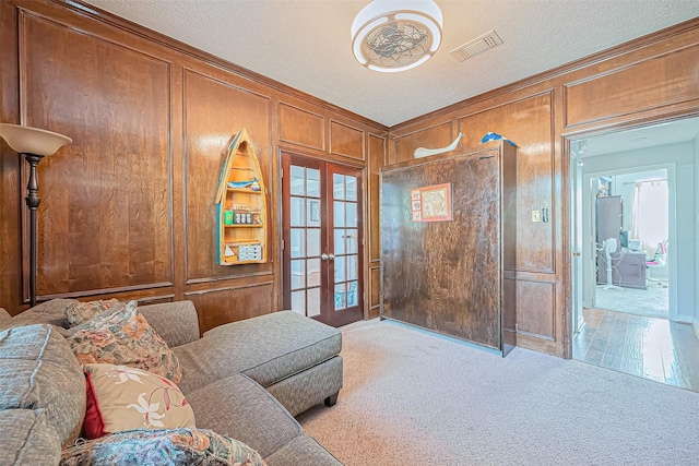 carpeted living area with wooden walls, french doors, visible vents, and a textured ceiling