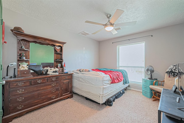 bedroom featuring a ceiling fan, light colored carpet, visible vents, and a textured ceiling