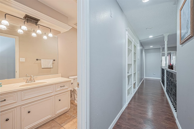 hallway with a sink, a textured ceiling, light wood-style floors, baseboards, and ornate columns