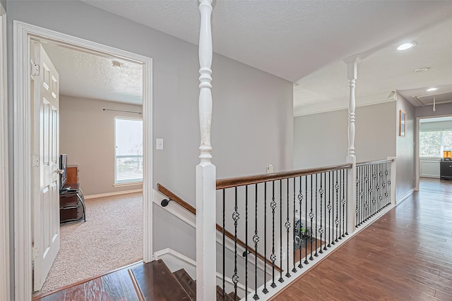 corridor with an upstairs landing, a textured ceiling, wood finished floors, baseboards, and attic access