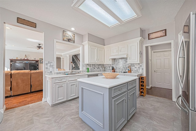 kitchen featuring gray cabinetry, a sink, a kitchen island, freestanding refrigerator, and light countertops