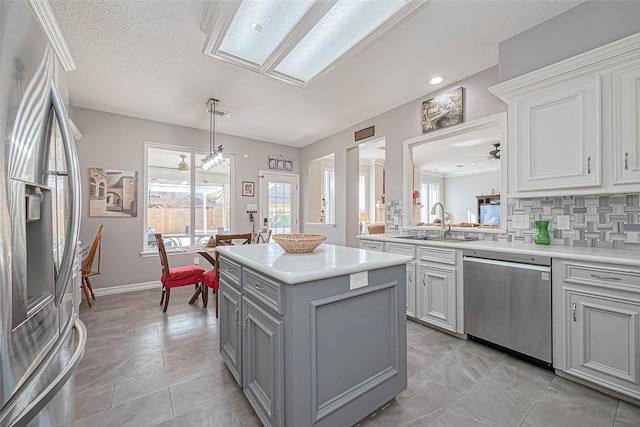 kitchen featuring gray cabinetry, a sink, stainless steel appliances, light countertops, and decorative backsplash