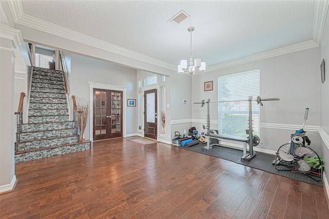 exercise room featuring visible vents, ornamental molding, a textured ceiling, hardwood / wood-style floors, and an inviting chandelier