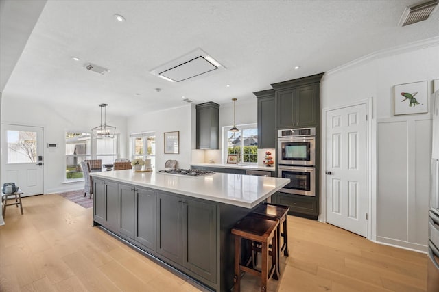 kitchen with visible vents, a kitchen island, light countertops, light wood-type flooring, and appliances with stainless steel finishes