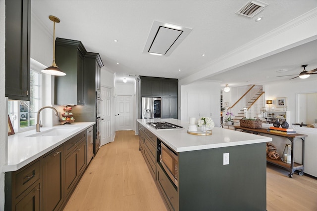 kitchen with a sink, a kitchen island, light wood-style floors, and appliances with stainless steel finishes