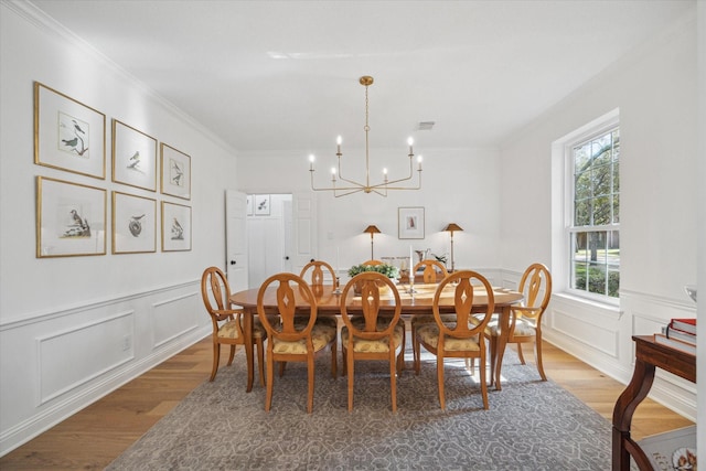 dining room featuring light wood finished floors, a wainscoted wall, an inviting chandelier, and ornamental molding