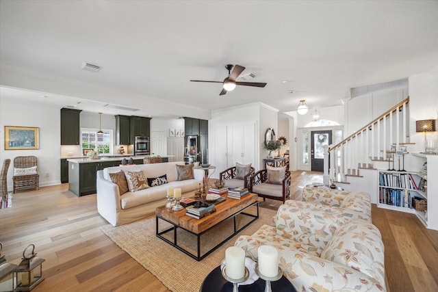 living room with light wood-type flooring, visible vents, and stairway