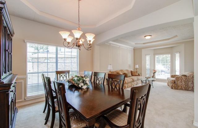 dining area featuring a tray ceiling, arched walkways, a decorative wall, a notable chandelier, and light colored carpet