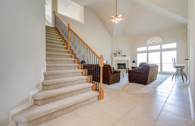 living room featuring high vaulted ceiling, light tile patterned floors, ceiling fan, stairs, and a tile fireplace