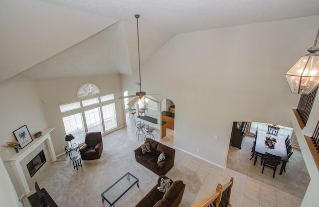 carpeted living area with tile patterned flooring, high vaulted ceiling, ceiling fan with notable chandelier, and a tile fireplace