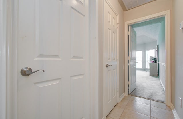 hall featuring light tile patterned floors, visible vents, light carpet, and baseboards