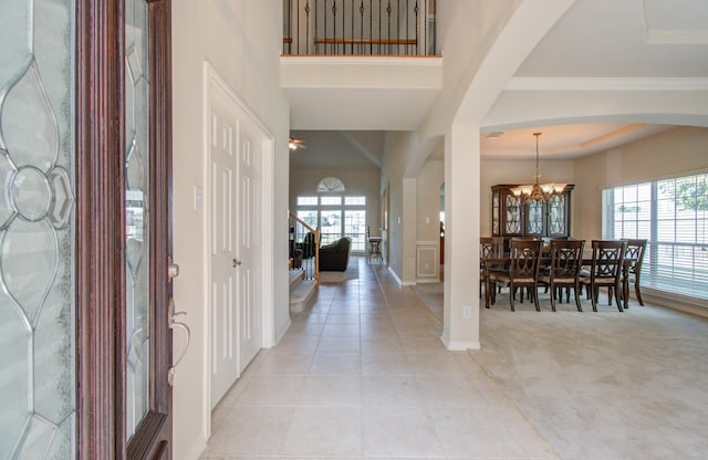 foyer featuring light colored carpet, light tile patterned floors, a high ceiling, arched walkways, and a notable chandelier