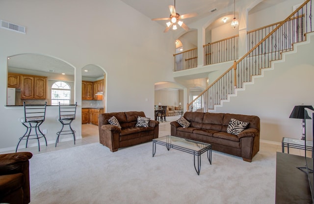 living area with visible vents, light carpet, arched walkways, a towering ceiling, and stairs