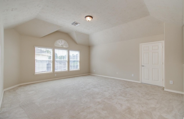 spare room featuring visible vents, a textured ceiling, baseboards, lofted ceiling, and light colored carpet