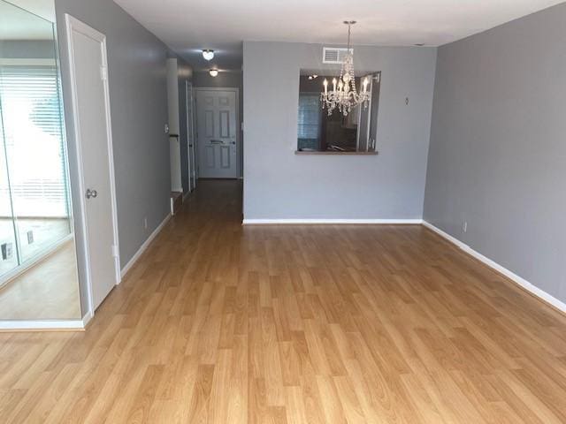 spare room featuring an inviting chandelier, wood finished floors, visible vents, and baseboards