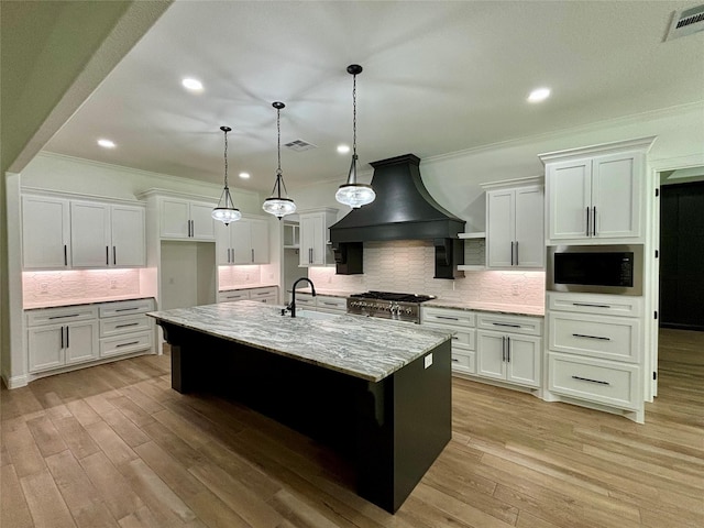 kitchen featuring premium range hood, built in microwave, light wood-type flooring, and visible vents