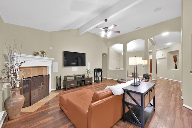 living area featuring visible vents, vaulted ceiling with beams, a tiled fireplace, wood finished floors, and arched walkways