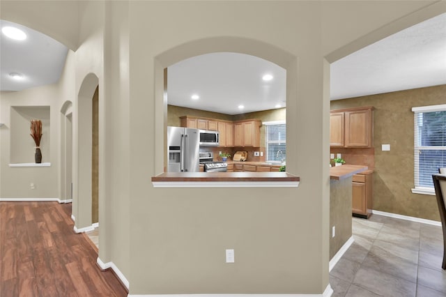 kitchen with a sink, recessed lighting, stainless steel appliances, arched walkways, and baseboards