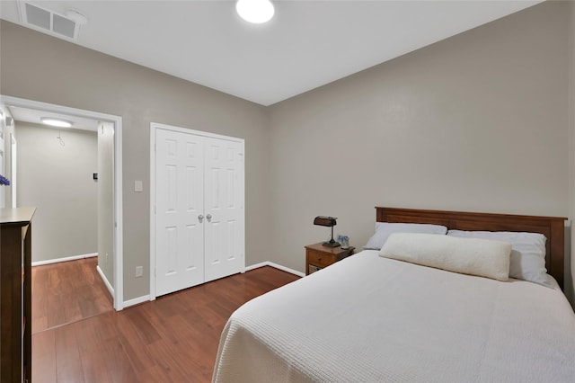 bedroom with wood finished floors, visible vents, a closet, and baseboards