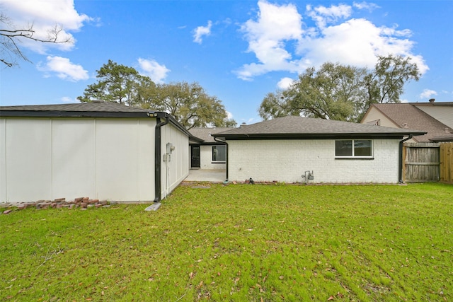 rear view of house featuring brick siding, a lawn, and fence