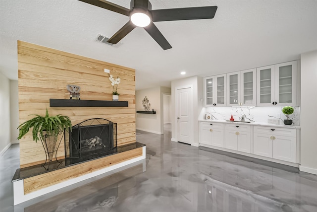 living room featuring a ceiling fan, finished concrete flooring, visible vents, baseboards, and a fireplace with raised hearth