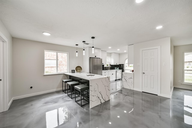 kitchen featuring dishwashing machine, white cabinetry, a peninsula, freestanding refrigerator, and a kitchen bar