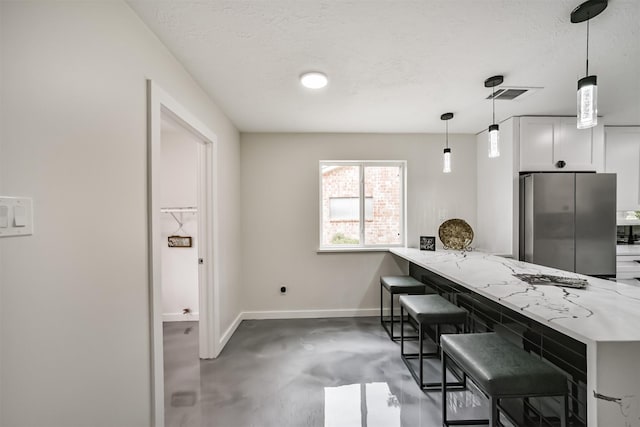 kitchen featuring visible vents, baseboards, concrete flooring, a kitchen breakfast bar, and freestanding refrigerator