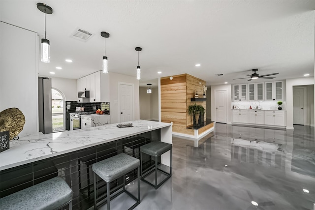 kitchen with visible vents, backsplash, white cabinetry, appliances with stainless steel finishes, and light stone countertops