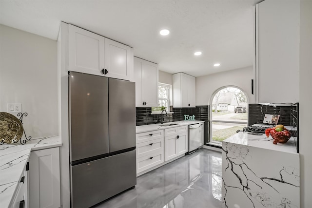 kitchen featuring backsplash, light stone counters, appliances with stainless steel finishes, white cabinets, and a sink