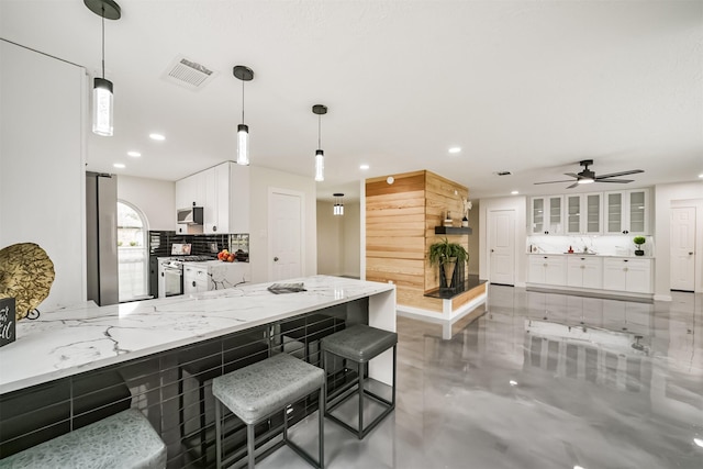 kitchen featuring light stone counters, visible vents, stainless steel appliances, decorative backsplash, and white cabinetry