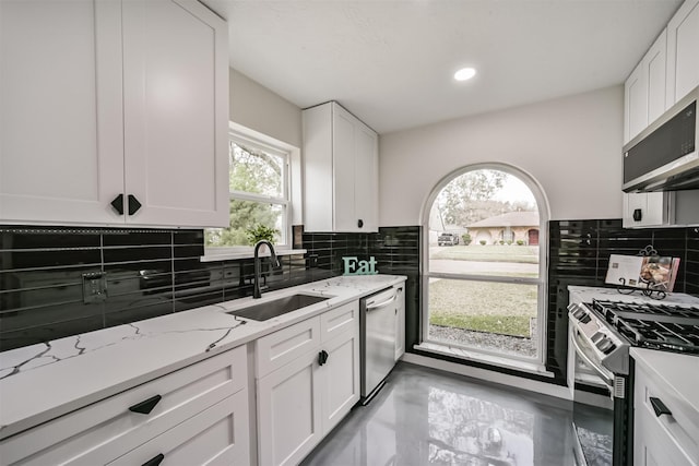 kitchen with backsplash, appliances with stainless steel finishes, white cabinetry, and a sink