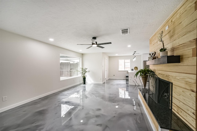 unfurnished living room with visible vents, baseboards, a fireplace with raised hearth, finished concrete floors, and a textured ceiling