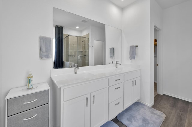 bathroom featuring wood finished floors, visible vents, baseboards, double vanity, and a stall shower