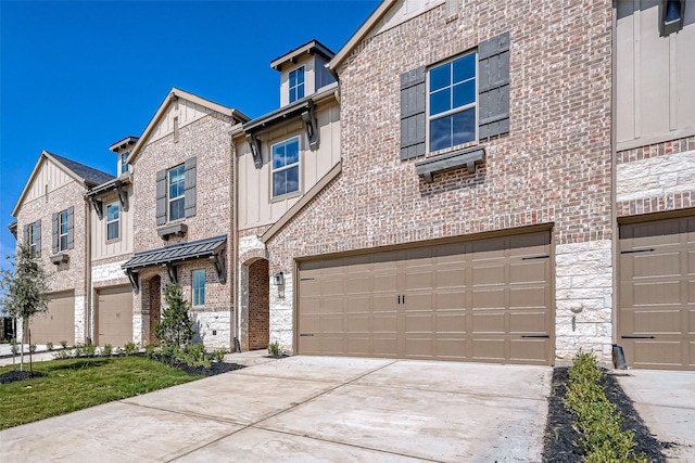 townhome / multi-family property featuring brick siding, board and batten siding, a garage, stone siding, and driveway