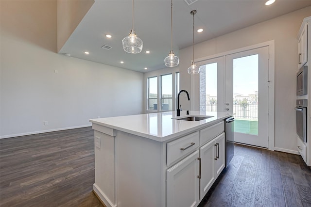 kitchen with dark wood-type flooring, a center island with sink, a sink, stainless steel appliances, and light countertops