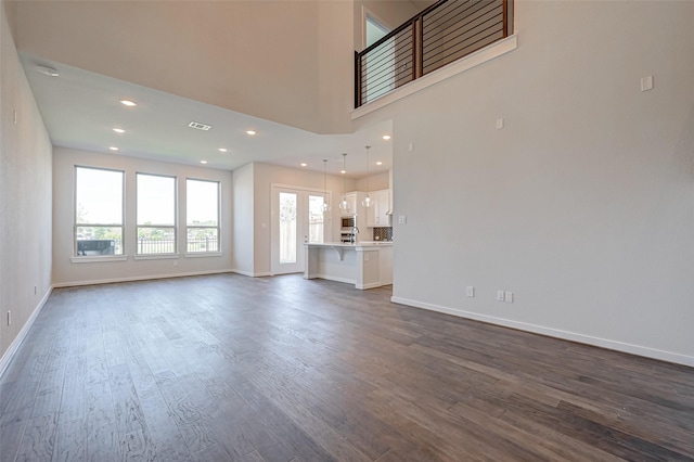 unfurnished living room featuring a wealth of natural light, baseboards, and dark wood finished floors