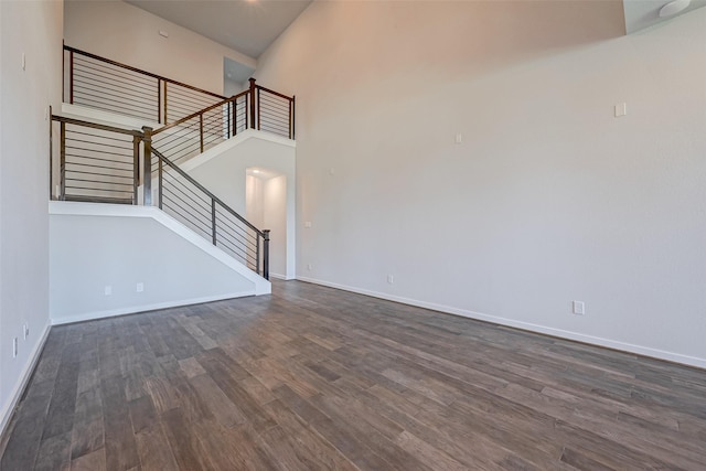 unfurnished living room featuring dark wood finished floors, a high ceiling, stairs, and baseboards