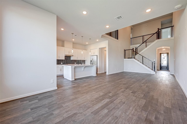 unfurnished living room with dark wood-style floors, visible vents, baseboards, recessed lighting, and stairs