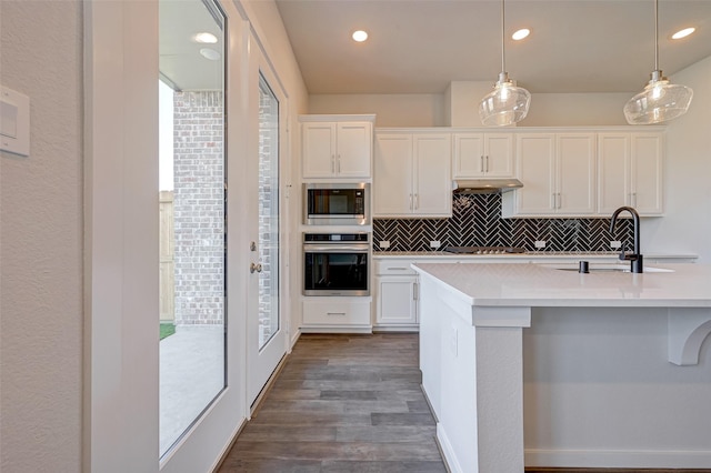 kitchen with tasteful backsplash, oven, built in microwave, light countertops, and a sink