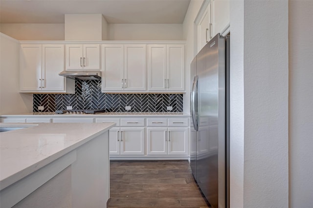 kitchen with backsplash, dark wood-type flooring, under cabinet range hood, freestanding refrigerator, and white cabinets