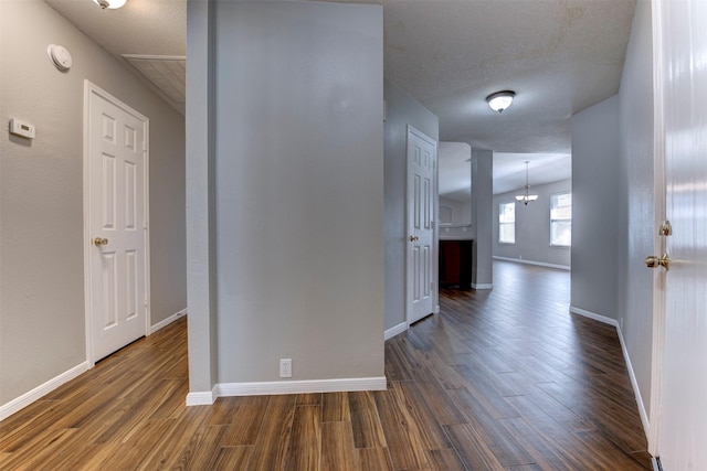 corridor with dark wood-style floors, a chandelier, a textured ceiling, and baseboards