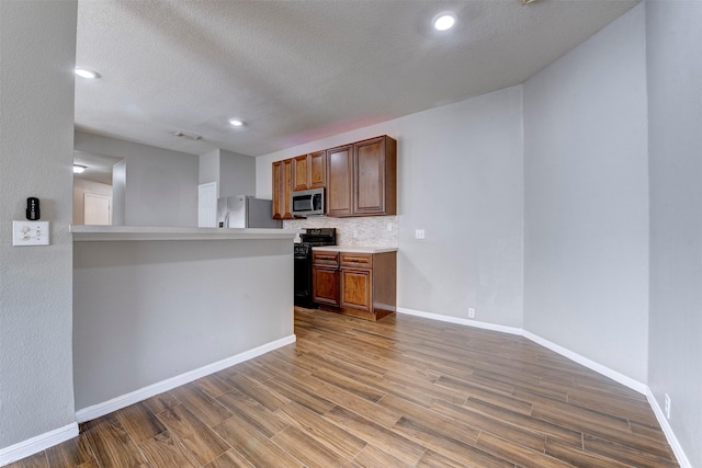 kitchen featuring baseboards, light countertops, decorative backsplash, wood finished floors, and stainless steel appliances