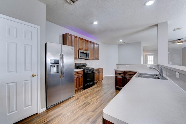 kitchen with light wood-style flooring, a sink, light countertops, appliances with stainless steel finishes, and a textured ceiling