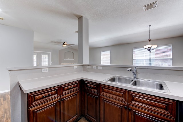 kitchen featuring visible vents, a sink, hanging light fixtures, light countertops, and ceiling fan with notable chandelier